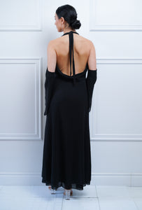 Femme debout et de dos portant une robe noire à dos ouvert et longues manches